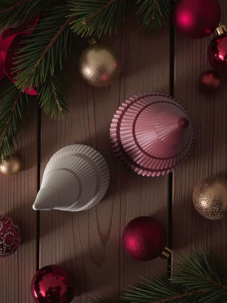 May include: A festive arrangement featuring Christmas ornaments and decorative objects. The image showcases red and gold baubles, along with two unique, cone-shaped ornaments in white and pink. Green pine branches add a seasonal touch to the wooden background.