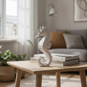 May include: A white seahorse sculpture sits on a light wood square table. The seahorse is the focal point, with a detailed, textured design. The table is in a living room setting, with books and a sofa in the background.