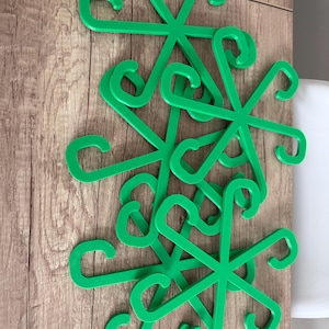 May include: A collection of bright green, star-shaped plastic hangers. Each hanger has six curved hooks extending from a central point. The hangers are arranged on a wooden surface, creating a visually appealing pattern.