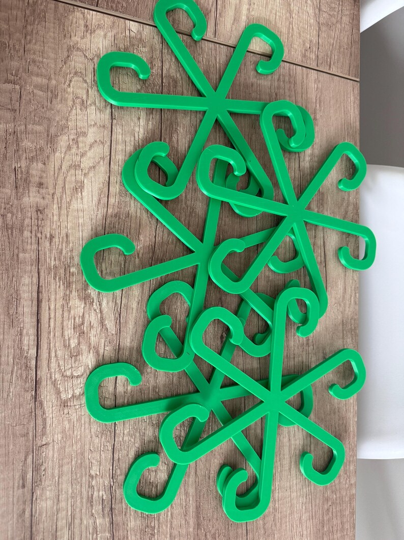 May include: A collection of bright green, star-shaped plastic hangers. Each hanger has six curved hooks extending from a central point. The hangers are arranged on a wooden surface, creating a visually appealing pattern.