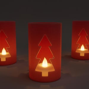 May include: Three red cylindrical candle holders with a Christmas tree cutout design. Each holder contains a small, flickering LED candle, creating a warm, inviting glow. The candle holders are arranged on a neutral surface.