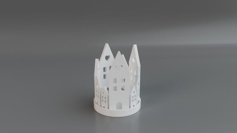May include: A white, cylindrical candle holder with a cut-out village design. The holder features various house shapes with windows and heart-shaped cutouts. The design is repeated around the circumference of the holder.