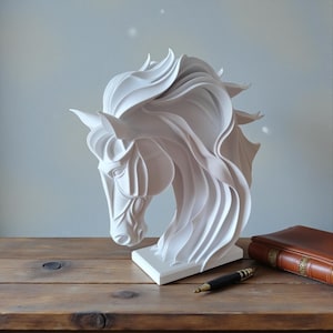 May include: A white sculpture of a horse's head with flowing mane and detailed facial features. The sculpture sits on a white base. A leather-bound book and a pen are on a wooden surface.