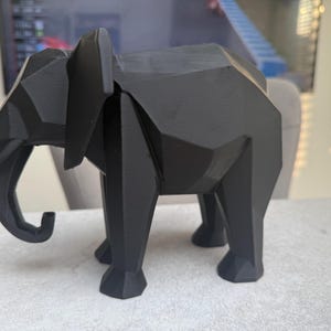 Op de afbeelding: Een zwarte geometrische olifant sculptuur. De sculptuur is gemaakt van een matzwart materiaal en heeft een facetontwerp. De olifant heeft grote oren, een slurf en vier poten. Dit decoratieve item is geschikt voor woondecoratie.