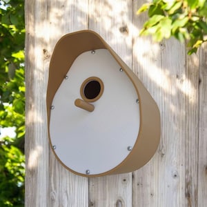 May include: A tan and white birdhouse with a rounded shape and a small entrance hole. The birdhouse is mounted on a wooden surface.