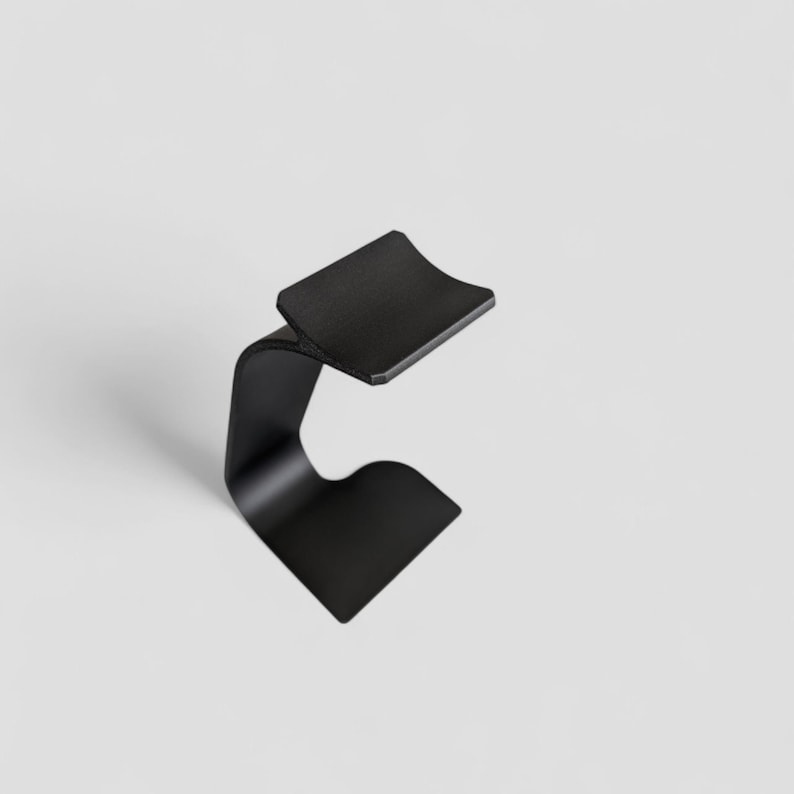 Peut inclure: Un support en m&eacute;tal noir minimaliste avec un design incurv&eacute;. Le support pr&eacute;sente un dessus plat et rectangulaire et une base incurv&eacute;e, cr&eacute;ant une esth&eacute;tique moderne et &eacute;l&eacute;gante. Le support est con&ccedil;u pour contenir un objet.