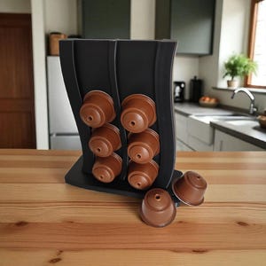 May include: A black coffee pod holder with a curved design, holding several brown coffee pods. The holder sits on a wooden surface, with a kitchen in the background.