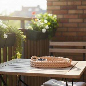 Puede incluir: Una bandeja redonda beige tejida con asas sobre una mesa de madera. La bandeja contiene un peque&ntilde;o cuenco de ar&aacute;ndanos. La mesa est&aacute; en un balc&oacute;n con flores y una pared de ladrillo al fondo.