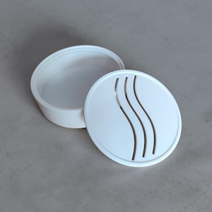 May include: A white, round container with a lid. The lid features three curved, vertical cutouts. The container is open, revealing its interior. The design is simple and modern, suitable for various storage purposes.
