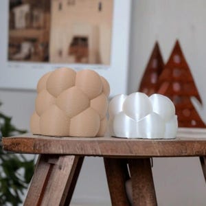 May include: Two bubble-shaped decorative planters. One is a light tan color, and the other is white. They are sitting on a rustic wooden table. The planters have a unique, textured design, perfect for small plants or succulents.