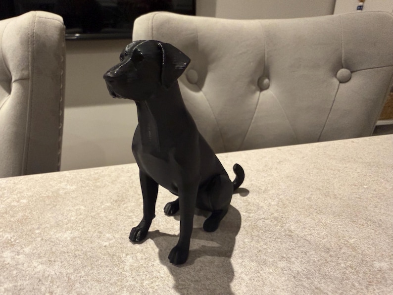 May include: A black dog figurine in a sitting position. The dog has a smooth, glossy finish and is positioned on a light-colored surface. The figurine is a decorative item, likely for home decor.