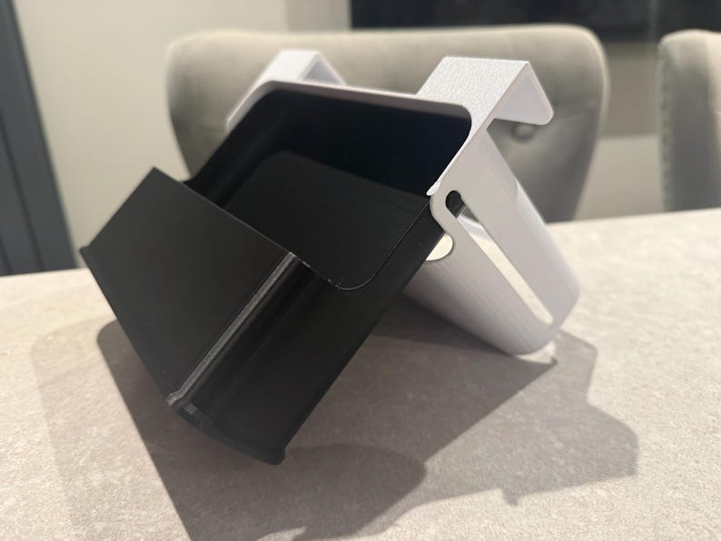 May include: A two-toned desk organizer with a black compartment and a white, angled support structure. The organizer is designed to hold items and has a modern, minimalist aesthetic. The black compartment is open and accessible.