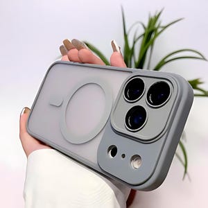 Puede incluir: Una funda gris para tel&eacute;fono con parte trasera transparente y m&oacute;dulo de c&aacute;mara gris. La funda tiene un &aacute;rea de carga magn&eacute;tica circular y un borde elevado alrededor de las lentes de la c&aacute;mara. La funda est&aacute; dise&ntilde;ada para proteger la c&aacute;mara y el cuerpo del tel&eacute;fono.