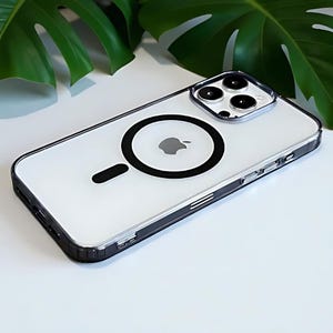 May include: Clear phone case with a black border and a black circular design on the back. The case has a built-in magnet and a clear back, showcasing the phone's design. The Apple logo is visible.