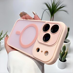 Puede incluir: Una funda de tel&eacute;fono rosa claro con protector de lente de c&aacute;mara. La funda tiene una parte trasera transparente con un dise&ntilde;o circular rosa y un marco rosa a juego alrededor de las lentes de la c&aacute;mara. La funda est&aacute; dise&ntilde;ada para proteger la c&aacute;mara del tel&eacute;fono.