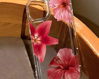 Può includere: Custodia trasparente per telefono con un design floreale di fiori di ibisco rosa. La custodia è trasparente, consentendo di vedere il colore del telefono. I fiori hanno petali dettagliati e un aspetto realistico.