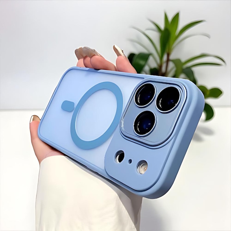 Puede incluir: Una funda de tel&eacute;fono azul claro con una parte trasera transparente y un dise&ntilde;o de anillo azul. La funda tiene un recorte para la c&aacute;mara con tres lentes y un flash. La funda la sostiene una persona.