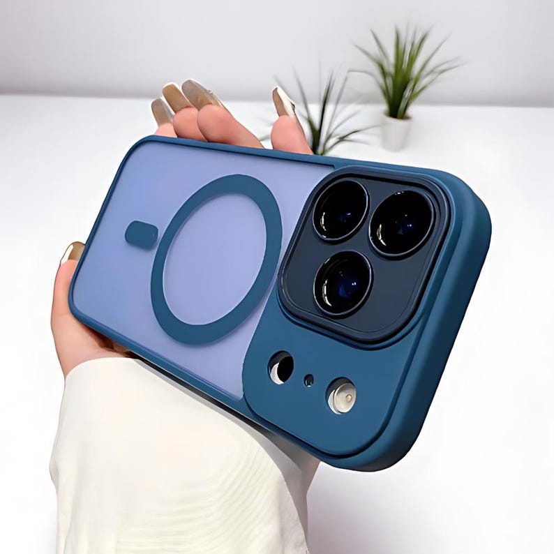 Puede incluir: Una funda de tel&eacute;fono azul y transparente con un protector de lente de c&aacute;mara. La funda tiene un anillo magn&eacute;tico circular y un m&oacute;dulo de c&aacute;mara azul oscuro con tres lentes. La funda se sostiene en una mano.