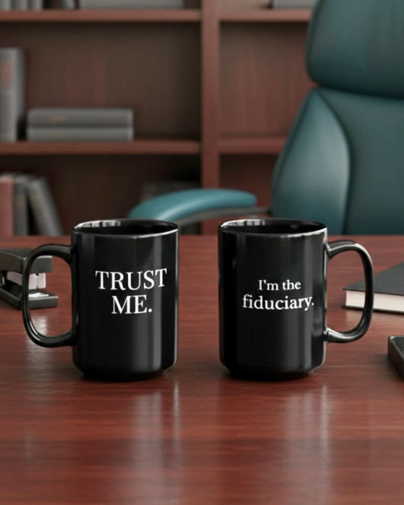 May include: Two black ceramic mugs with white text on a wooden desk. One mug says "TRUST ME." and the other says "I'm the fiduciary." The mugs have a glossy finish and are in a professional setting.