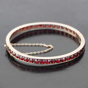 Pode incluir: Um bracelete de prata com uma fila de pedras preciosas vermelhas ao redor da borda.