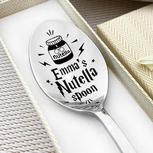 May include: A silver spoon engraved with "Emma's Nutella spoon" and a Nutella jar illustration. The spoon is presented in a cream-colored gift box with a matching ribbon. The spoon is approximately 7 inches long.