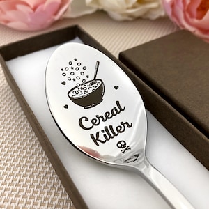 Op de afbeelding: Een roestvrijstalen lepel met de woorden "Cereal Killer" gegraveerd op de lepelbak. De lepel heeft een afbeelding van een kom ontbijtgranen met sterren en harten. Gepresenteerd in een bruine geschenkverpakking.