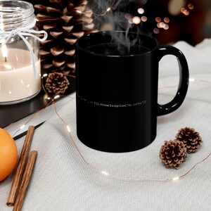 May include: A black coffee mug with the text "for _ in ().throw(Exception("No Coffee"))" in green. The mug is on a white surface with decorative items, including pine cones and a candle.
