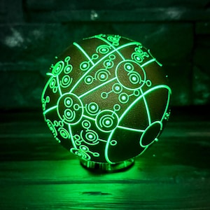May include: A spherical lamp emitting a bright green glow, featuring intricate, interconnected circular and linear patterns etched across its dark surface. The light radiates from within, highlighting the detailed geometric design.