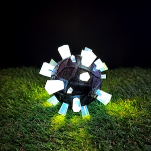 May include: A spherical object with a dark, textured surface featuring multiple protruding, translucent white crystal-like spikes that emit a bright glow, casting a soft light onto the surrounding area.