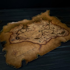 Peut inclure: Une carte détaillée et vieillie de la province de Bordeciel, avec des détails géographiques complexes et une rose des vents. La carte a un aspect vieilli et vieilli avec des bords brûlés, et le texte "Province of Skyrim" est visible.