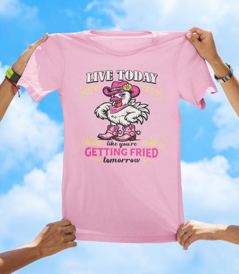 Puede incluir: Una camiseta rosa claro con un gr&aacute;fico de un pollo blanco que lleva un sombrero de vaquero rosa, un pa&ntilde;uelo rosa y botas de vaquero rosas. El texto dice LIVE TODAY like you're GETTING FRIED tomorrow en letras negras y rosas.