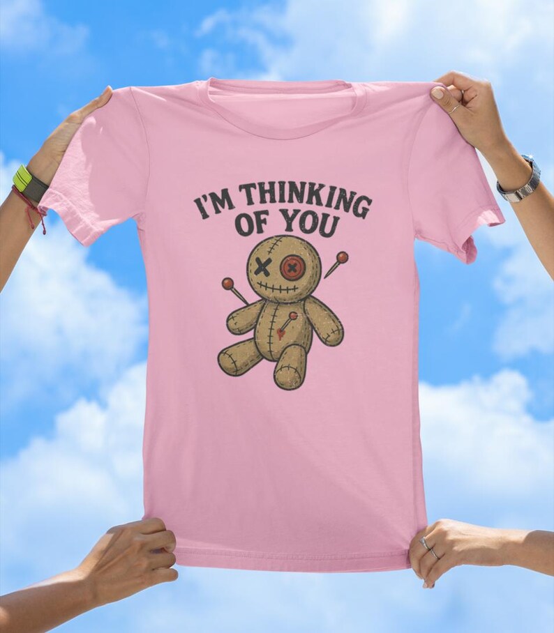 May include: Pink t-shirt featuring a voodoo doll graphic and the text "I'm thinking of you".