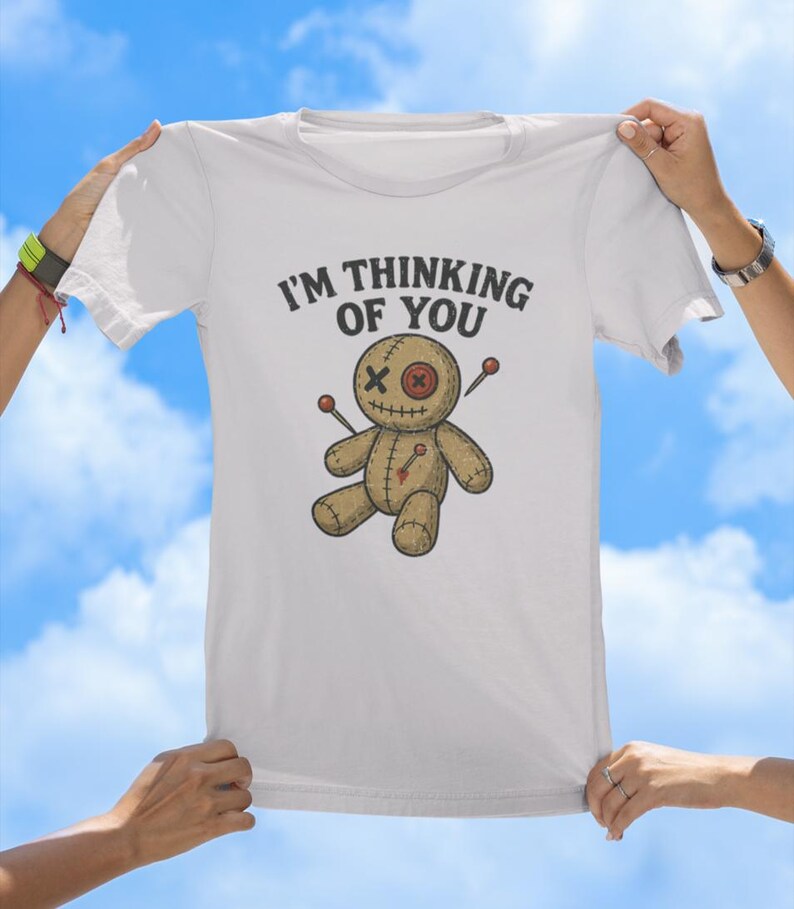 May include: White t-shirt featuring the text "I'm thinking of you" and a cartoon voodoo doll with needles sticking out of it.