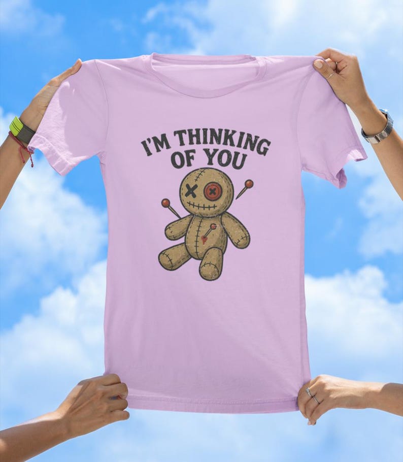 May include: A pink t-shirt featuring the text "I'm thinking of you" and a cartoon voodoo doll with needles sticking out of it.