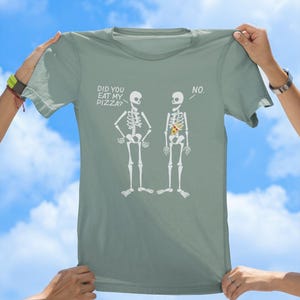 May include: A light green t-shirt with a humorous graphic of two skeletons. One skeleton asks "Did you eat my pizza?" and the other skeleton replies "No."