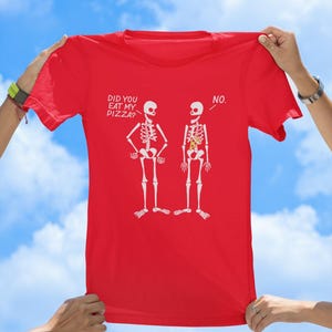 May include: Red t-shirt with a graphic of two skeletons. One skeleton has a slice of pizza in its ribcage. The text on the shirt reads "Did you eat my pizza?" and "No."
