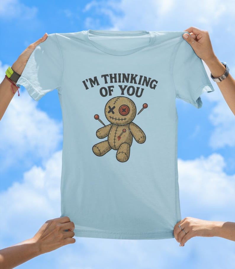 May include: Light blue t-shirt featuring a voodoo doll graphic and the text "I'm thinking of you".