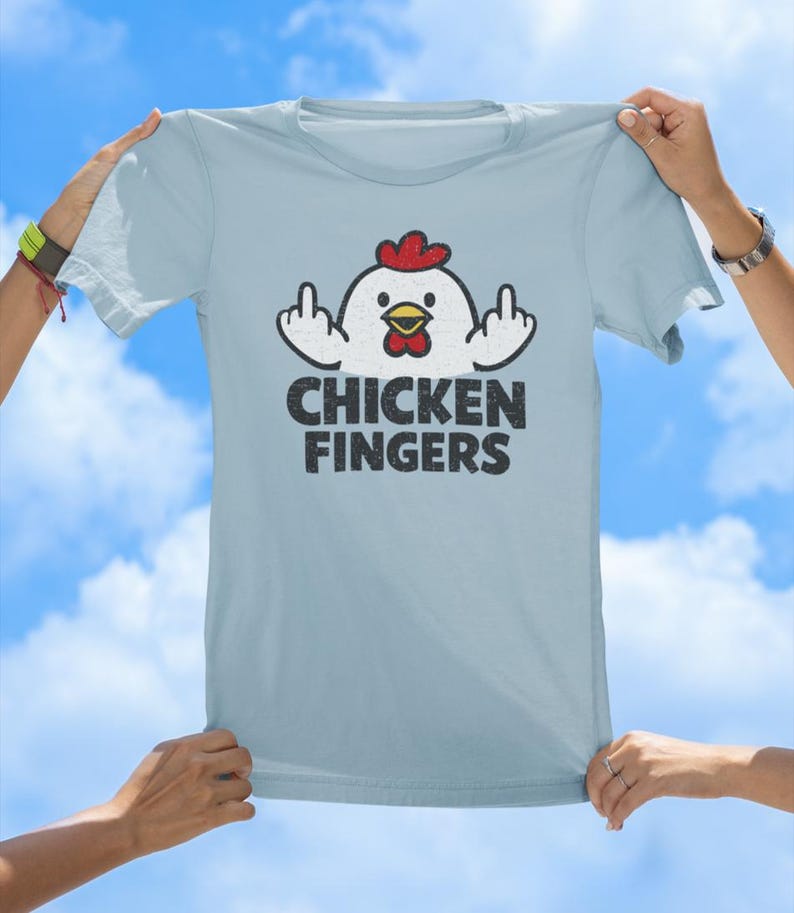 May include: A light blue t-shirt featuring a graphic of a white chicken with a red comb and yellow beak. The chicken is shown with its wings raised, displaying middle fingers. Below the graphic, the text CHICKEN FINGERS is printed in black.