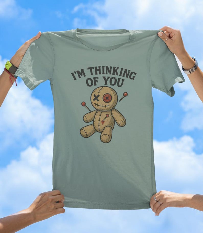 May include: A light blue t-shirt featuring a voodoo doll graphic and the text "I'm thinking of you".