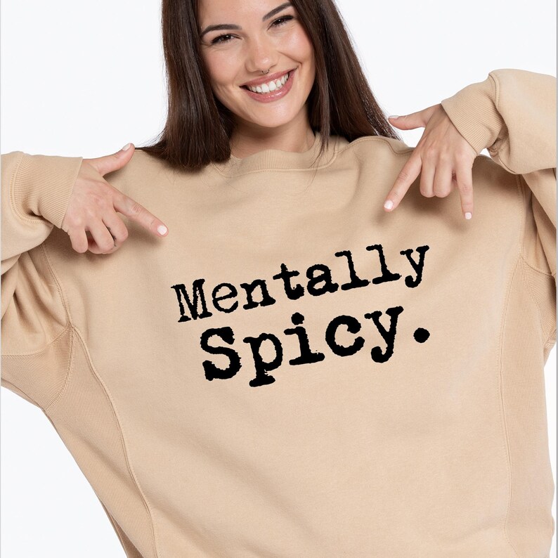 May include: A tan sweatshirt with the text "Mentally Spicy" in black, bold letters. The sweatshirt is a neutral color and has a classic crew neck design.