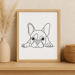 May include: A framed black and white line drawing of a French Bulldog. The dog is depicted in a minimalist style, with large eyes and floppy ears. The artwork is displayed in a light-colored wooden frame.