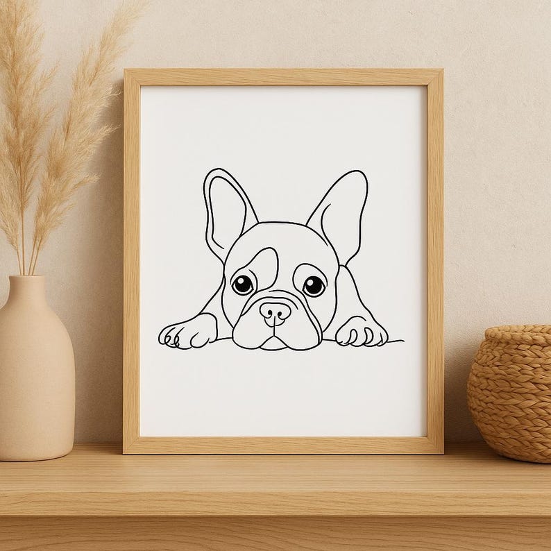 May include: A framed black and white line drawing of a French Bulldog. The dog is depicted in a minimalist style, with large eyes and floppy ears. The artwork is displayed in a light-colored wooden frame.