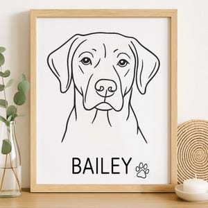 May include: A framed black and white line drawing of a dog's face. The dog's name, "BAILEY," is printed in a bold font below the image, along with a paw print symbol. The artwork is displayed in a light wood frame.