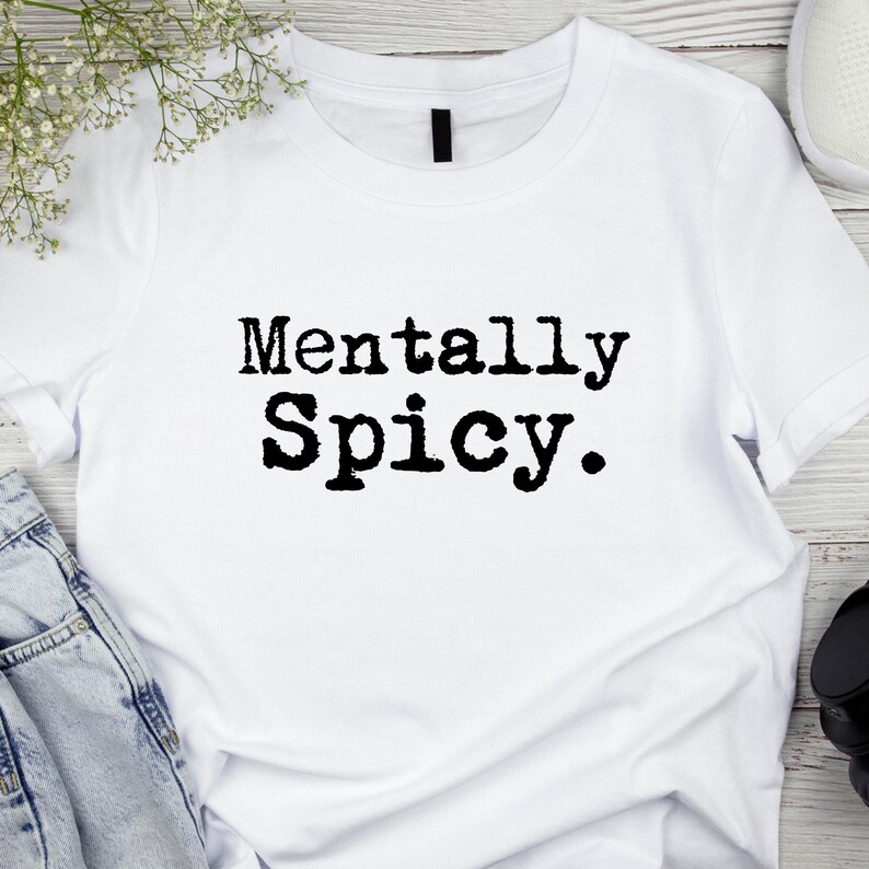 May include: White t-shirt with the phrase "Mentally Spicy" printed in black, bold letters. The shirt is made of a soft material and is suitable for casual wear. The design is simple and eye-catching.