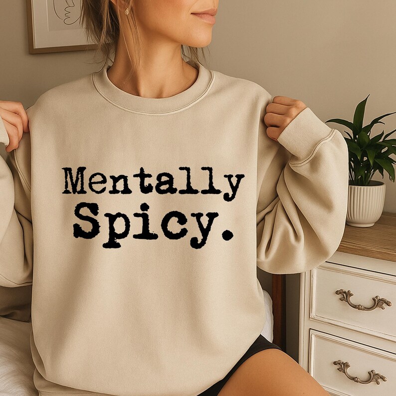May include: Beige crewneck sweatshirt with the text "Mentally Spicy" in a bold, black font. The sweatshirt is a neutral color, and the text is centered on the front. The style is casual and comfortable.