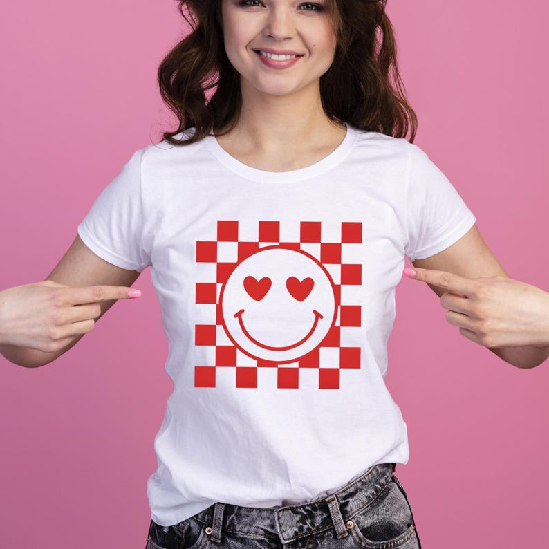 Op de afbeelding: Wit T-shirt met een rood-wit geblokt patroon en een smiley. De smiley heeft hartvormige ogen. Het T-shirt is een klassieke ronde hals.