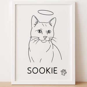 May include: A framed art print featuring a black and white line drawing of a cat with a halo. The cat's name, "SOOKIE," is printed below, along with a paw print. The artwork is set against a white background.