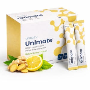 Op de afbeelding: Een witte doos Unicity Unimate yerba mate drankmix met de woorden "Natural Lemon Flavor". Twee gele zakjes en een in plakjes gesneden citroen met gember en groene bladeren staan voor de doos.