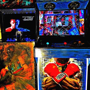 Könnte beinhalten: Eine Nahaufnahme eines individuell lackierten Arcade-Schranks mit einem blauen und schwarzen Sockel. Der Schrank zeigt ein farbenfrohes Bild eines Boxers mit roten Handschuhen und dem Text "Ryu" auf der Vorderseite. Der Schrank hat auch ein Schwarzweißbild eines Terminator-Charakters auf der linken Seite und ein Schwarzweißbild eines Videospielcharakters auf der rechten Seite.