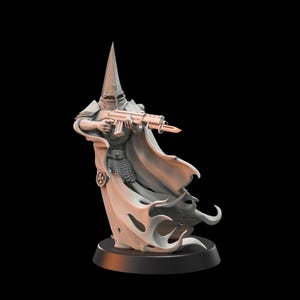 May include: A gray figurine of a robed figure wearing a pointed helmet and holding a rifle with a bayonet. The figure has a flowing cape and is standing on a black base. The figurine has a chainmail chest piece.